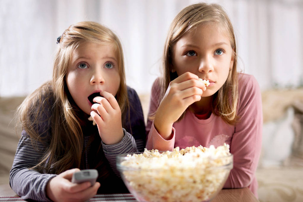 two young girls eat popcorn and watch TV - Foto, Imagem