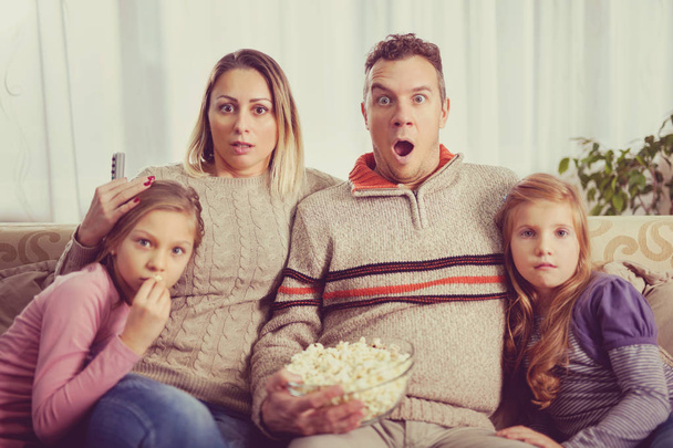 Beautiful young parents and their children are watching TV, eati - Фото, изображение