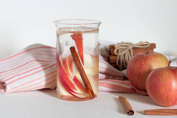 Glass with fresh apple water and cinnamon sticks on light table - Photo, Image