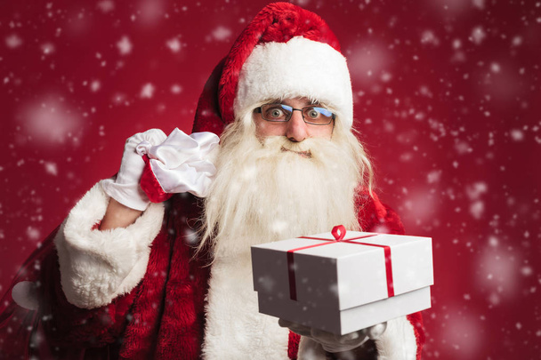 Санта Клаус держит сумку на плече и предлагает подарок
 - Фото, изображение