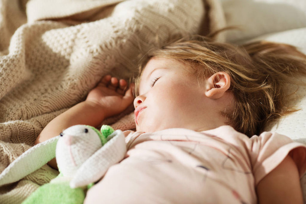 Sleeping little girl. Carefree sleep little baby with a soft toy on the bed. Close-up portrait of a beautiful sleeping child on knitted blanket. Sweet dreams - Photo, Image