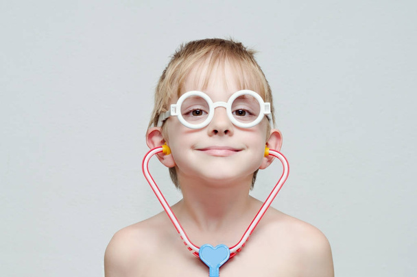 Cute boy is playing doctor. Toy glasses and phonendoscope. Portrait - Photo, Image