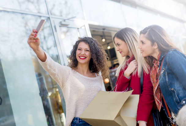 giovani donne felici scattare foto su smartphone all'aperto vicino edificio di vetro moderno
 - Foto, immagini