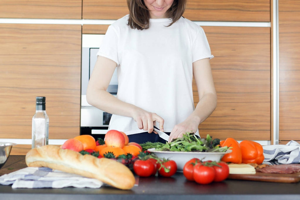 Young woman preparing healthy vegetables salad in the modern kitchen. Woman cutting some vegetables - Zdjęcie, obraz