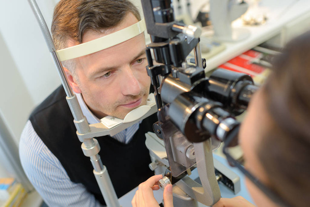 optician in surgery giving man eye test - Foto, Imagem