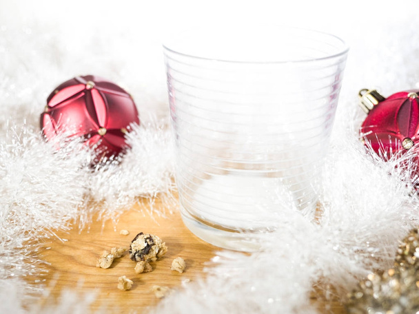 Lege melkglas en cookie kruimels met rode Kerst ornamenten opleggen van witte garland vakantie achtergrond - Foto, afbeelding