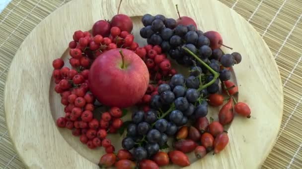 Rotating in wooden plate northern grapes, wild rose hips,apples and rowan berries on bamboo mat - Footage, Video