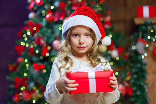 Little girl sitting by the tree holding a Christmas gift In the  - Foto, immagini