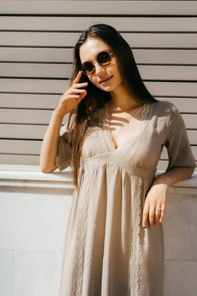 A girl in summer clothes and sunglasses leans against a wall in the street - Foto, Imagem