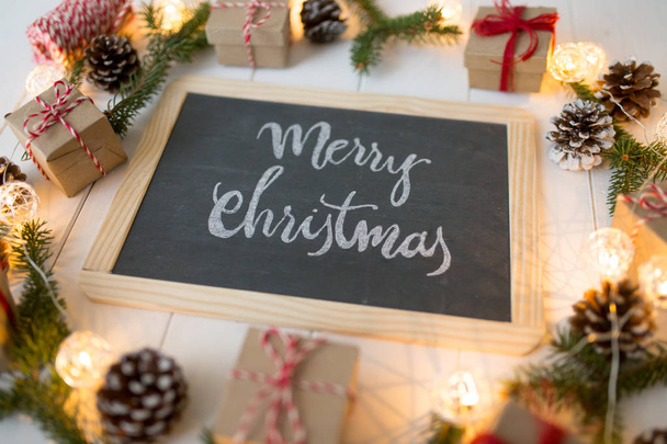 Christmas background with signboard and inscription, spruce, gift box and scroll on wooden boards. - Photo, Image