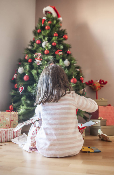 Niña abriendo sus regalos bajo el árbol de Navidad
 - Foto, imagen