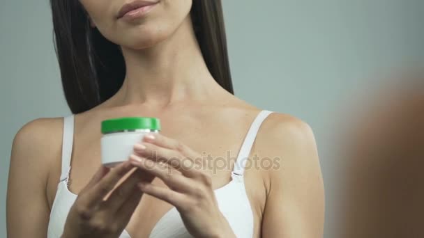 Young woman holding tub with face cream, opening and applying it, anti-aging - Materiał filmowy, wideo