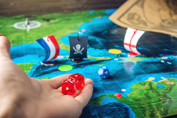 Hand throwing red dice on the world map of the playing field handmade Board games with a pirate ship - Photo, Image