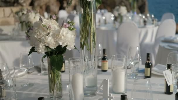 Белые цветы в вазе расставлены на столах к празднованию морем
. - Кадры, видео