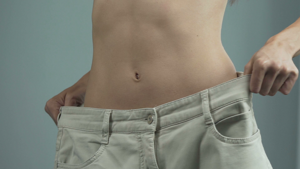 Atraktivní fit žena nošení a držení nadměrné kalhoty, tenké tónovaný tělo - Záběry, video