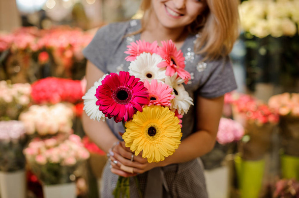 Smiling florist in a grey dress holding a beautiful colorful bouquet of flowers - Fotó, kép