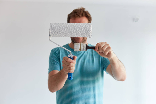 Smiling man holding a brush and a roller in front of him - Photo, image