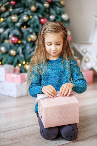 Ένα μικρό κορίτσι ανοίγει ένα δώρο στο πρωί Χριστουγέννων. Έννοια νέων Ναι - Φωτογραφία, εικόνα