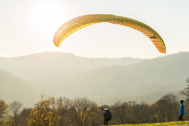 the guy is flying on a yellow parachute. wild beautiful nature, sunny weather, mountain view - Фото, изображение