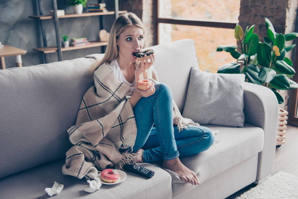 Beautiful blonde woman sitting on couch in living room under bla - Фото, изображение