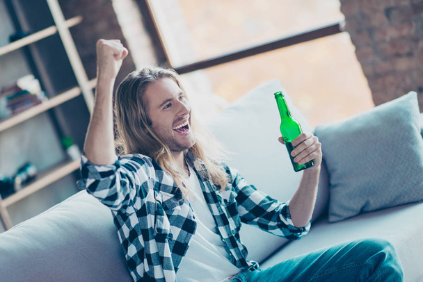Yeah! Cheerful young man drinking beer in front of TV. He is tri - Фото, изображение