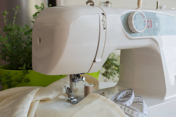 Machine à coudre coud tissu couleur écru, accessoires de couture autour
 - Photo, image