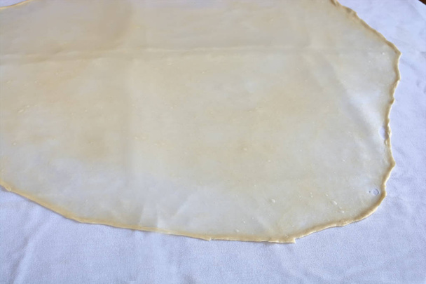 Homemade Phyllo or strudel dough on a home table cloth, ready for banitsa, apple strudel, baklava, burek, pie or other kind of traditional pastry - Photo, Image