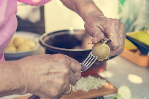 Closeup of elderly hands peaing potatoe. - Фото, изображение