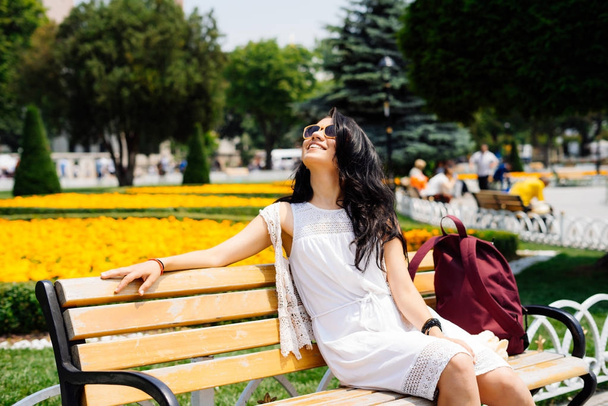 A beautiful girl rests on a bench in Istanbul, enjoying the sun. Flowers on the background - Foto, Imagem