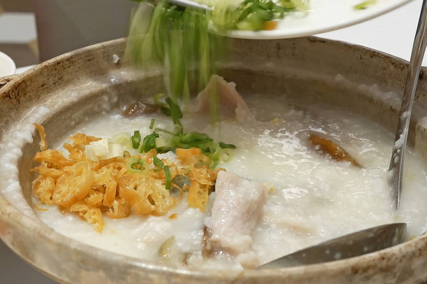 Primer plano de la gente vertiendo cebolla verde dentro de carne de cerdo picada congee con huevo conservado en la mesa
 - Foto, imagen