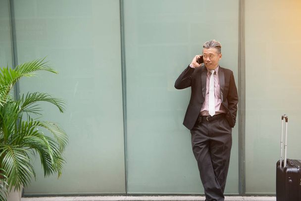 aasialainen vanhempi liikemies matkustaa puhelimen kanssa
 - Valokuva, kuva