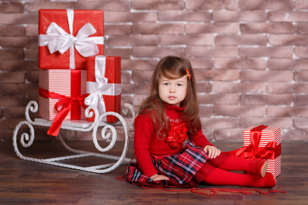 Young brunette dolly lady girl stylish dressed in red pullover sweater chequers check tartan skirt strap shoes smiling posing sitting in studio winter sledge jumper with pout lips and pink cheeks. - Foto, afbeelding