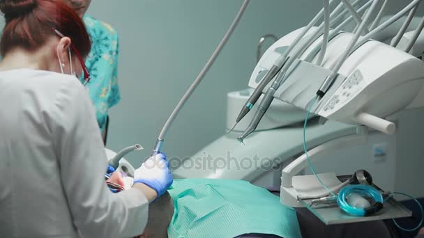 The dentist and nurse repairing a tooth of a patient man. The use of bormashenko to drill teeth and remove tooth decay and sealing. - Materiał filmowy, wideo