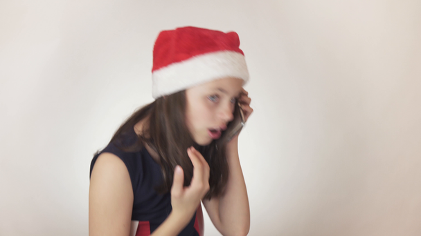 Mooie Stout meisje tiener in een kerstman hoed communiceert emotioneel op de smartphone op witte achtergrond stock footage video. - Video
