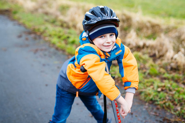 Cute preschool kid boy riding on scooter in park - Foto, afbeelding