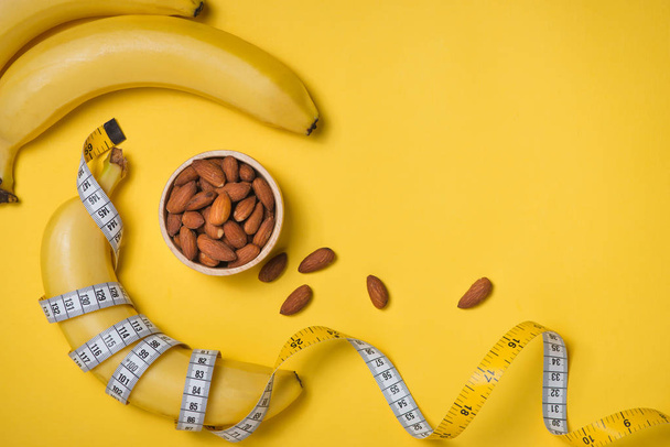 Измерительная лента обернутая вокруг банана с миндалем на желтом фоне, Концепция диеты
. - Фото, изображение