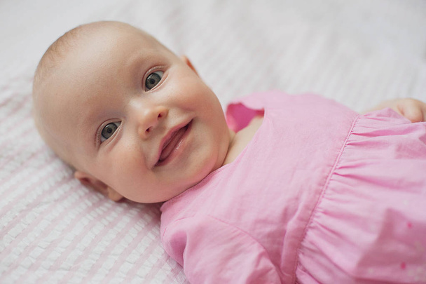 Cute baby girl in pink dress lies on white backgroun. Close-up portrait, smiling baby - Valokuva, kuva