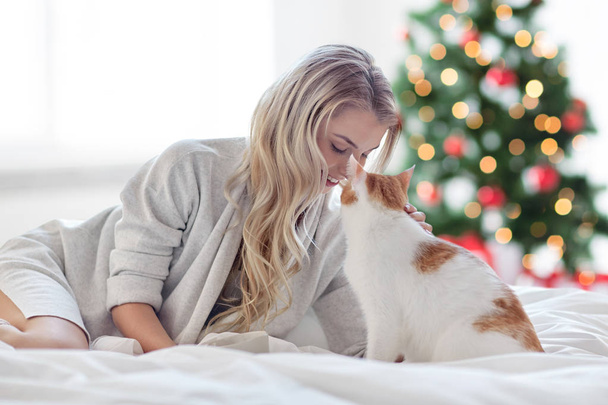 Szczęśliwa młoda kobieta z kotem w łóżku na Boże Narodzenie - Zdjęcie, obraz