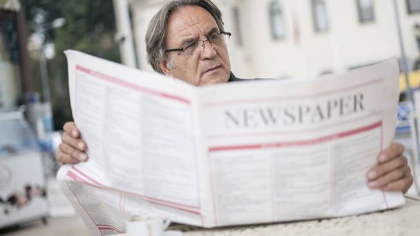 年配の男性が屋外で新聞を読む - 写真・画像