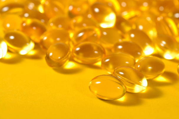 Omega-3 rybí tuk olej kapsle zblízka na žlutém podkladu. - Fotografie, Obrázek