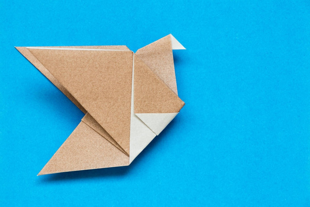 Papel de origami marrón en forma de ave voladora sobre fondo azul
 - Foto, Imagen