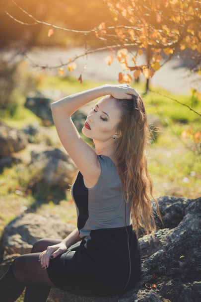 ブロンド毛秋のジャケットに身を包んだセクシーな素晴らしい女性女の子気の利いたスタイリッシュなふくれっ面の赤い唇を中央公園春の森林牧草地でカメラに座っているポーズの顔を作る - 写真・画像
