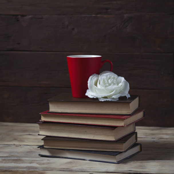 Rose bud, books and a red cup. Composition on a wooden backgroun - Foto, afbeelding