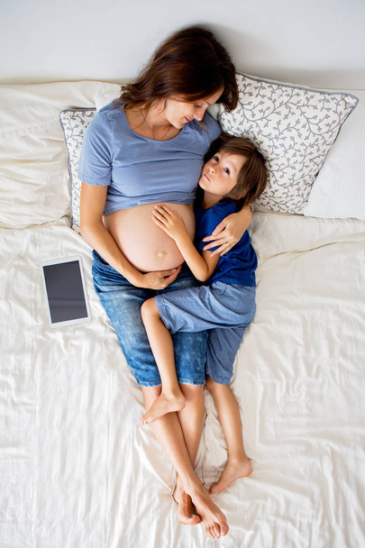 Mladá těhotná žena a její dítě, ležící v posteli - Fotografie, Obrázek