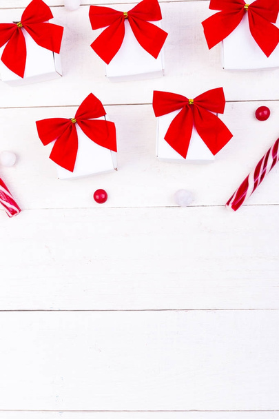 Різдвяні подарунки, білі маленькі коробки з червоним бантом та цукерками на білому дерев'яному тлі. Пласка лежала. Веселого Різдва
. - Фото, зображення