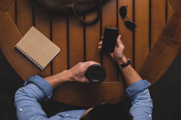 ο άνθρωπος με τον καφέ να πάμε χρησιμοποιώντας το smartphone - Φωτογραφία, εικόνα