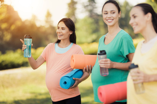 Three pregnant girls posing in a park with yoga mats in hand and sports bottles - Foto, immagini