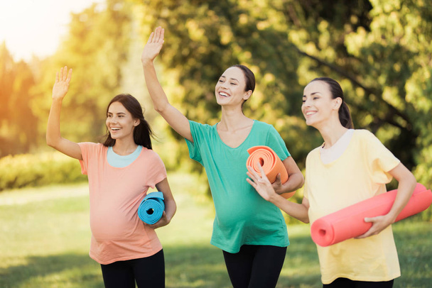 Three pregnant girls posing in a park with yoga mats in hand. They smile and have fun - Foto, Imagem