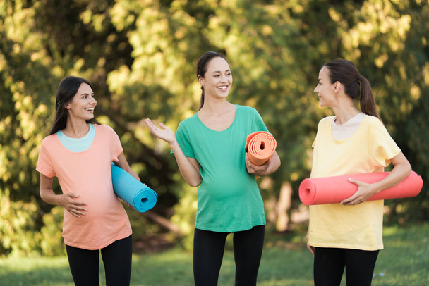 Three pregnant girls posing in a park with yoga mats in hand. They smile and have fun - Zdjęcie, obraz