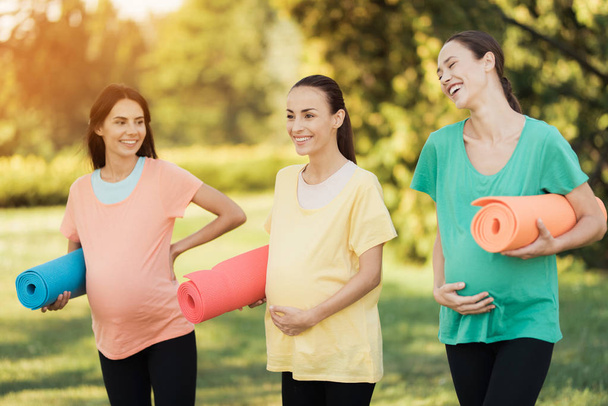 Three pregnant girls posing in a park with yoga mats in hand. They smile and have fun - Valokuva, kuva